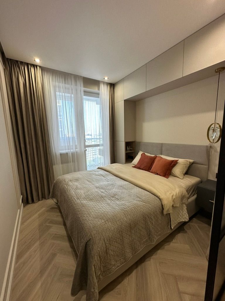Modern bedroom with a large bed, neutral bedding, and herringbone wood floors.